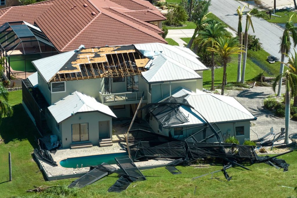 A large house with a destroyed roof and pool cage from hurricane damage in Florida.